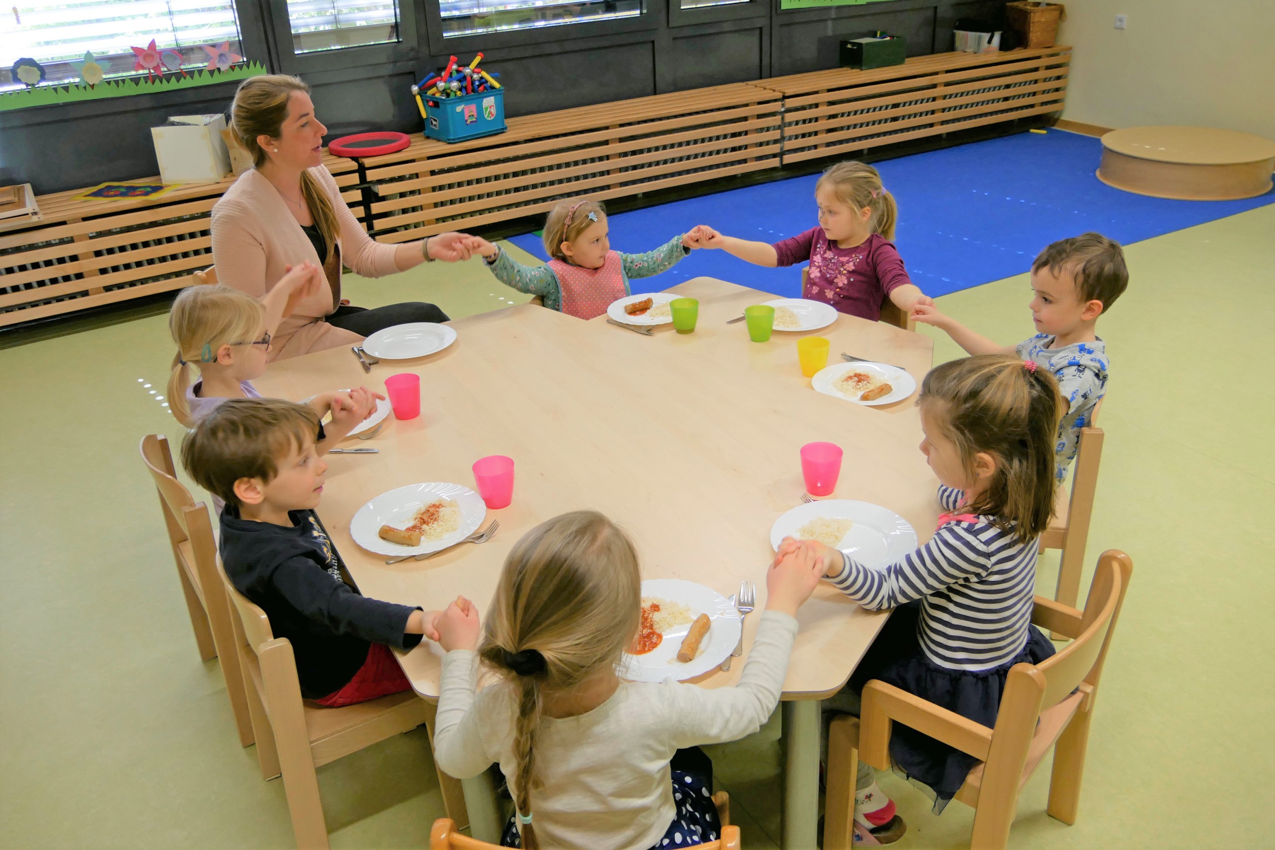 Kinder sitzen an einem Tisch im Kreis beim Mtitagessen
