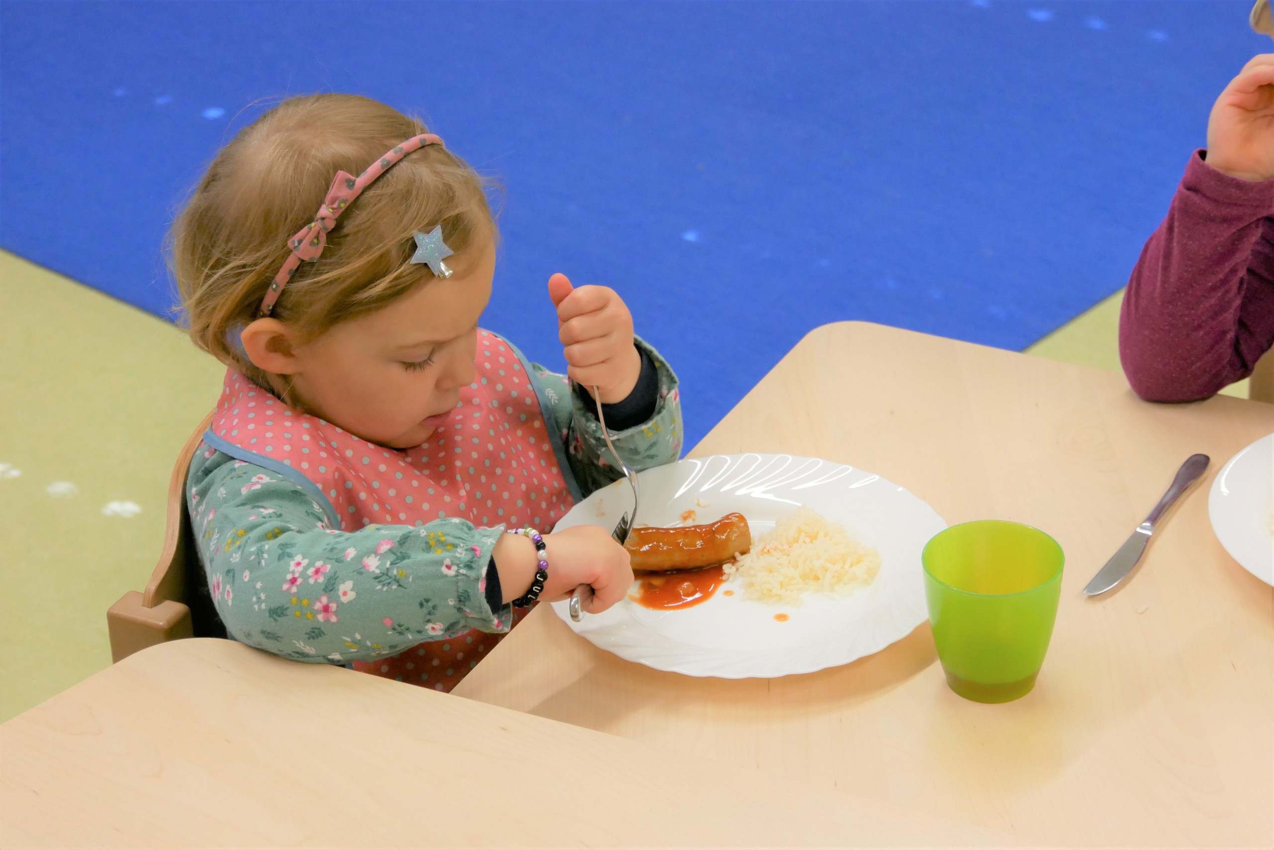 Kind schneidet selbständig das Mittagessen auf dem eigenen Teller klein