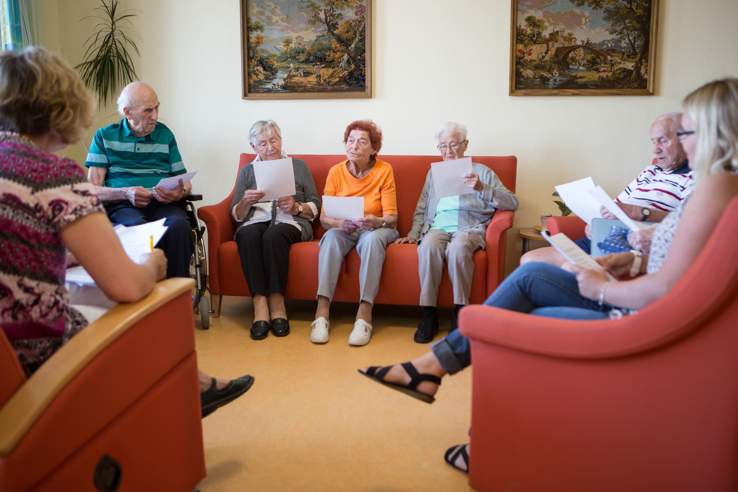 Mehere Personen sitzen im Kreis auf Sofas und haben Liedzettel in der Hand