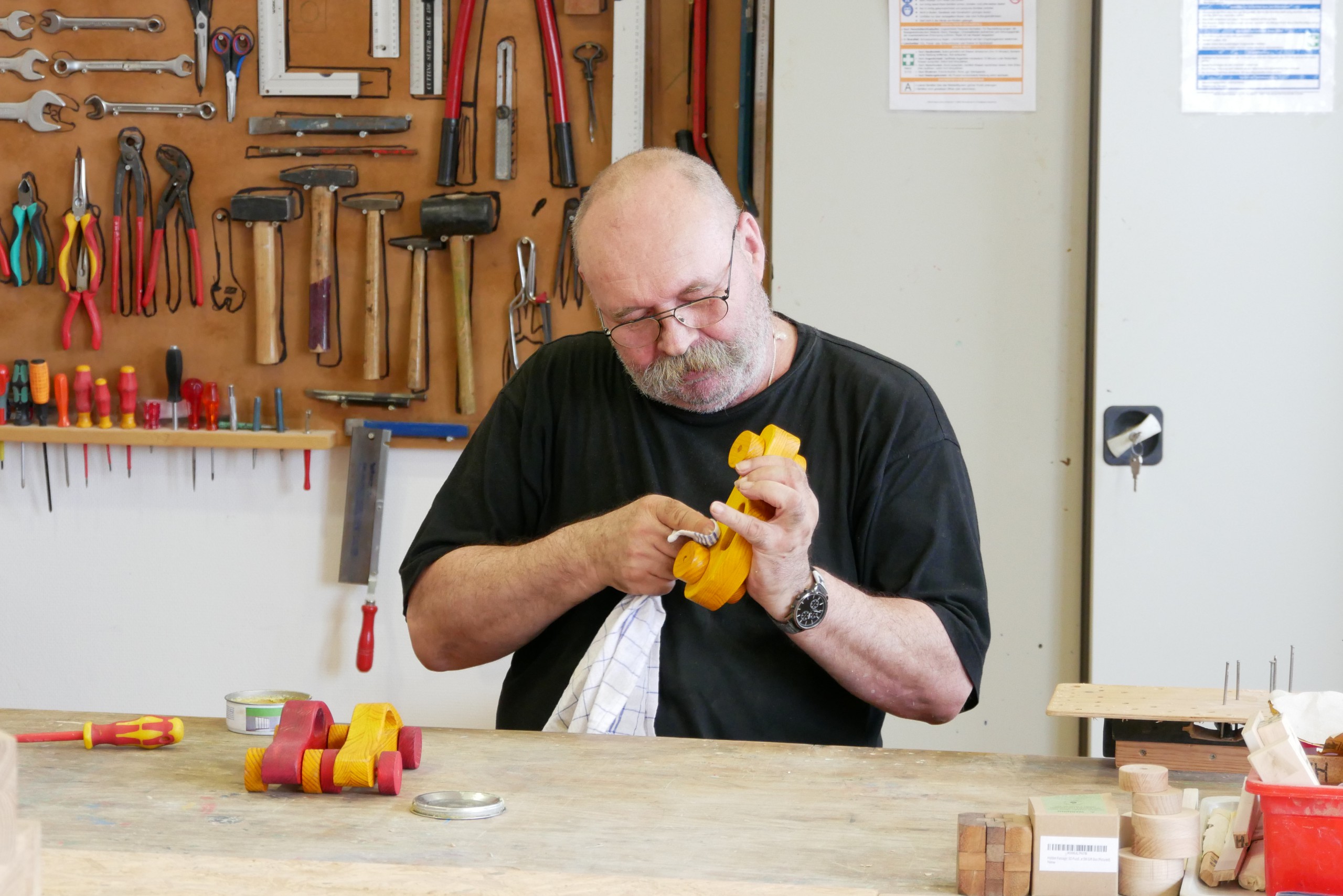 Eine Person arbeitet in einer Werkstatt mit Schmirgelpapier an einem Holzauto